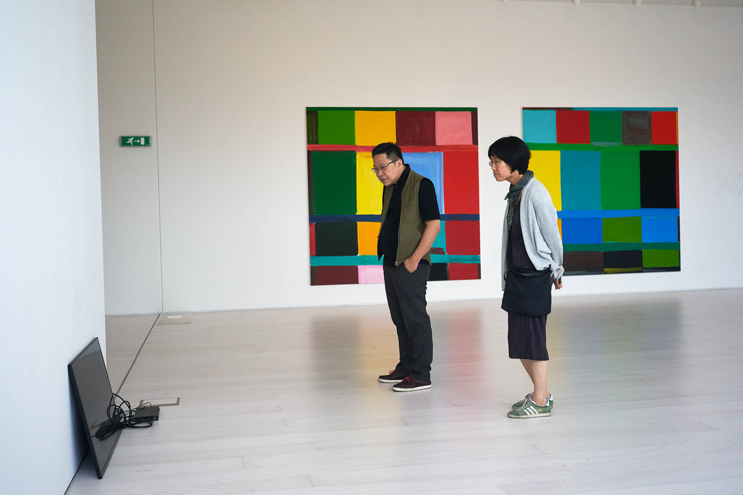 Two visitors watching video documentation of a performance by Marie Cool and Fabio Balducci; in the background, works by Stanley Whitney, National Museum of Contemporary Art, Athens, 2017